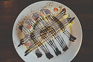 Pancakes with bananas and chocolate caramel sauce,Topping with whip cream and strawberry on table