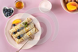 Pancakes with berries and honey on a pink pastel background, top view, copy space.