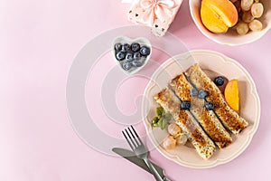 Pancakes with berries and honey on a pink pastel background, top view, copy space.