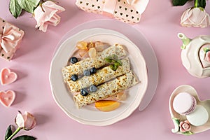 Pancakes with berries and honey on a pink pastel background, top view.