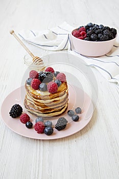 Pancakes with berries and honey on a pink plate, side view.