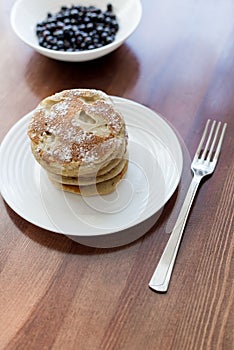 Pancakes with berries and powdered sugar in a white plate are on the table