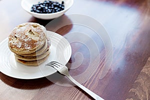 Pancakes with berries and powdered sugar in a white plate are on the table