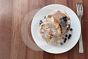 Pancakes with berries and powdered sugar in a white plate are on the table