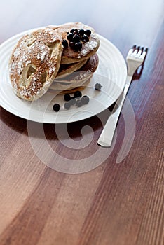 Pancakes with berries and powdered sugar in a white plate are on the table