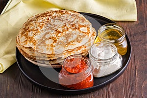 Pancakes on black plate. Fillings-sour cream, red caviar, honey. Pancake day. Russian tradition in the last week before Easter,