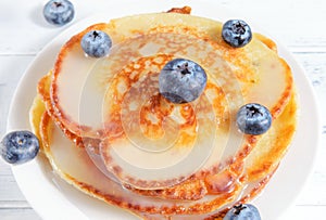 Pancakes with blue blueberry berries on a plate on a light background