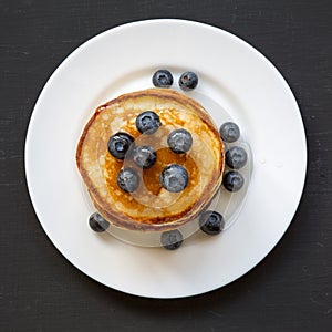 Pancakes with blueberries and honey on white plate on dark wooden table, overhead view. Flat lay, top view