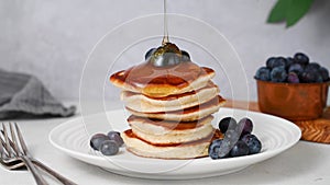 Pancakes with blueberries. Pouring honey or maple syrup over stack of pancakes