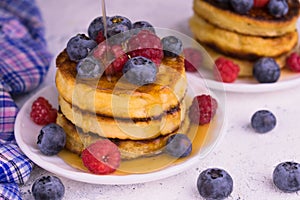 Pancakes with blueberries, raspberries and maple syrup on a white plate. Close-up.