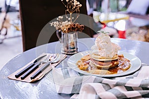 Pancakes with caramel-banana syrup topping with whip cream and mint leaves. With spoon, fork and knife, in blue plate over fabric.