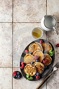 Pancakes in ceramic plate with berries, mint leaves, honey and forks, top view
