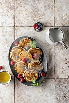 Pancakes in ceramic plate with berries, mint leaves and honey, top view