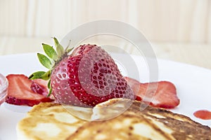 Pancakes with cheese and strawberries and sauce on a white dish against wood background. Delicious cheese pancake and strawberries