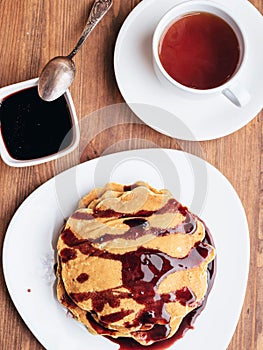 Pancakes with cherry jam on a white table. a cup of tea.