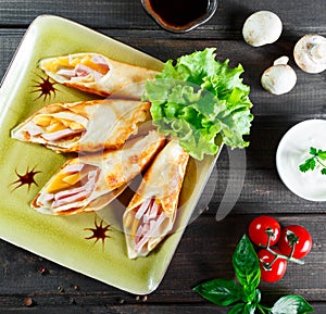 Pancakes with chopped ham and cheese, decorated with lettuce on dark wooden background close up.