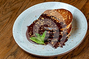Pancakes covered with chocolate on a blue plate with a mint leaf