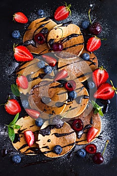 pancakes with fresh berries and chocolate sauce on black background