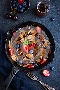 Pancakes with fresh berries and chocolate sauce on pan, black ba