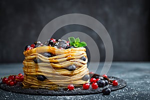 Pancakes with fresh berries and maple syrup on dark background
