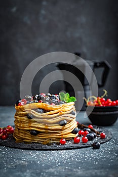 Pancakes with fresh berries and maple syrup on dark background