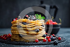 Pancakes with fresh berries and maple syrup on dark background