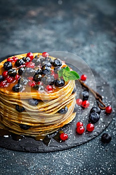 Pancakes with fresh berries and maple syrup on dark background