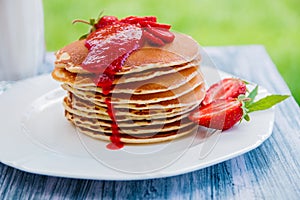 Pancakes with fresh strawberry and jam, near glass milk on white plate wooden background in garden or nature . Stack of th