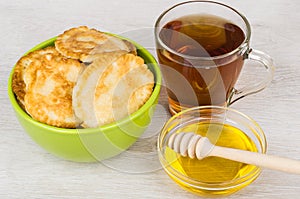 Pancakes in green bowl, honey, wooden stick and tea