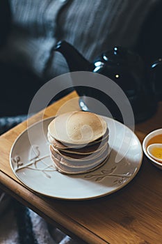 Pancakes with honey on wooden tray in cozy room.