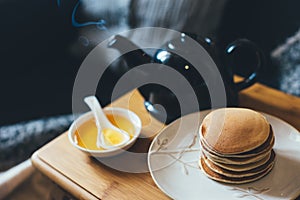 Pancakes with honey on wooden tray in cozy room.