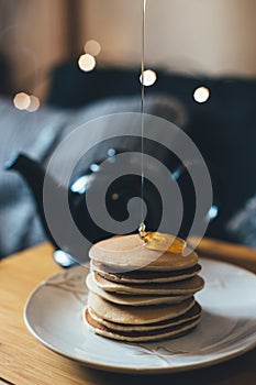 Pancakes with honey on wooden tray in cozy room.