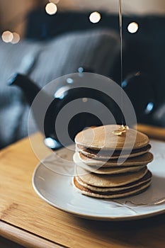 Pancakes with honey on wooden tray in cozy room.