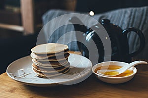 Pancakes with honey on wooden tray in cozy room.