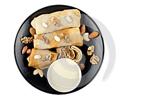 Pancakes with nuts and condensed milk on black plate isolated on white background