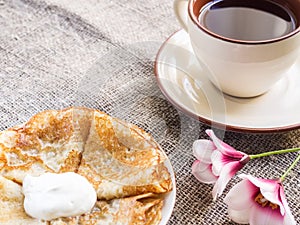 Pancakes, a plate with sour cream and a cup with red tea on a table