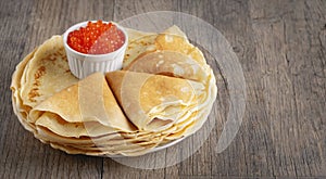 Pancakes with red caviar on a wooden table, with copy space for tex