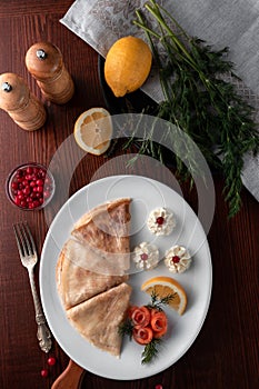 Pancakes with red fish, lemon and cranberries on a white plate, table served in restaurant in rustic style, concept of russian