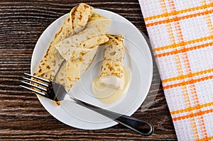 Pancakes rolls with condensed milk, fork in plate, napkin on table. Top view