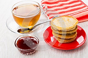 Pancakes on saucer, tea, spoon, red napkin, bowl with jam
