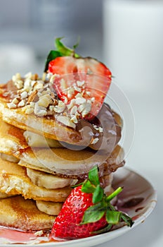 Pancakes stacked with bananas, strawberries and nuts, topped with chocolate and strawberry sauce