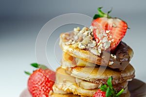Pancakes stacked with bananas, strawberries and nuts, topped with chocolate and strawberry sauce