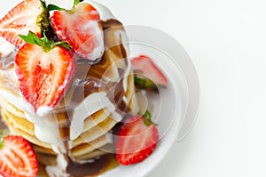 Pancakes stacked with strawberries, topped with  chocolate sauce and yoghurt