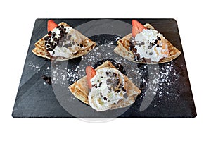 Pancakes with strawberries chocolate and cream on a black board isolated on white background