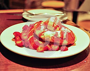 Pancakes strawberries with vanilla ice cream in a white plate.