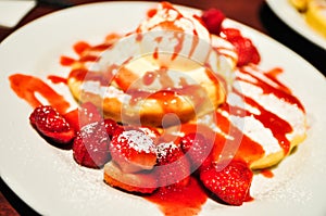 A Pancakes strawberries with vanilla ice cream in a white plate.