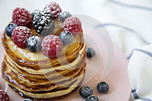 Pancakes with variety of berries and honey in pink plate