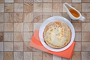 Pancakes on a white plate with a waffle orange towel, sauce-boat with honey maple syrup
