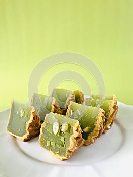 Pandan moon cake with seeds cut into eighths , green background. Vertical.