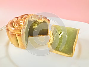 Pandan seeds moon cake with a portion cutout on pink background.